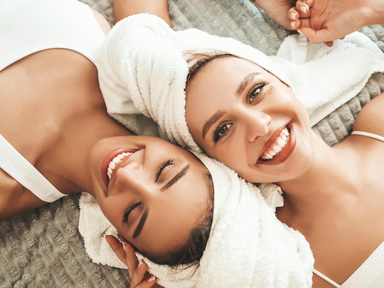 two women with towels on their head lay on the back an laugh