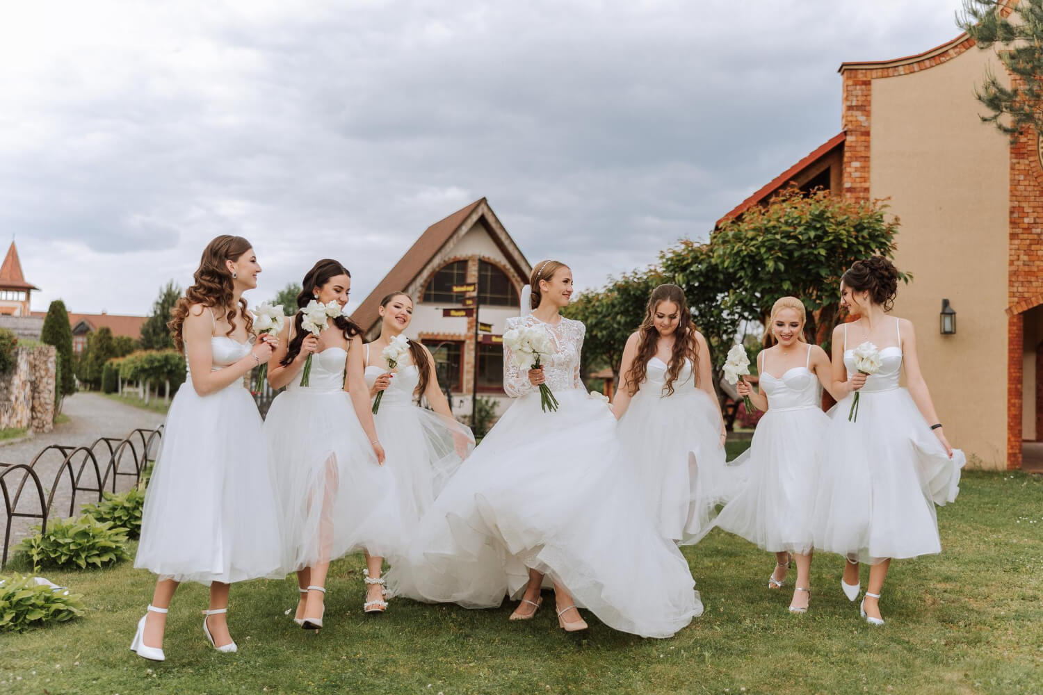 the bride and her six bridesmaids all dressed in white and holding small white flower bouquets walk together outside