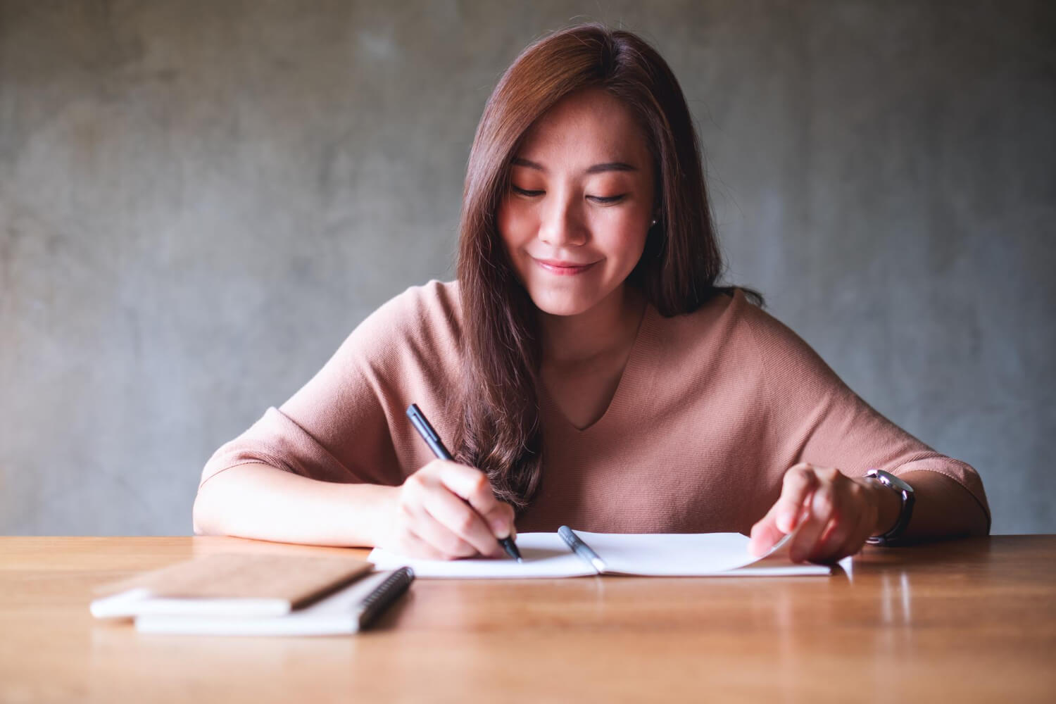 a woman smiling and sitting on a table and writing something in a notebook