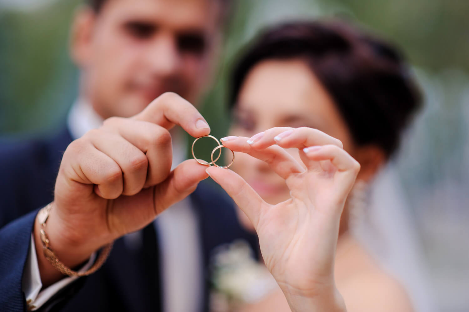 bride and groom both holding their ring between pointing finger and thumb