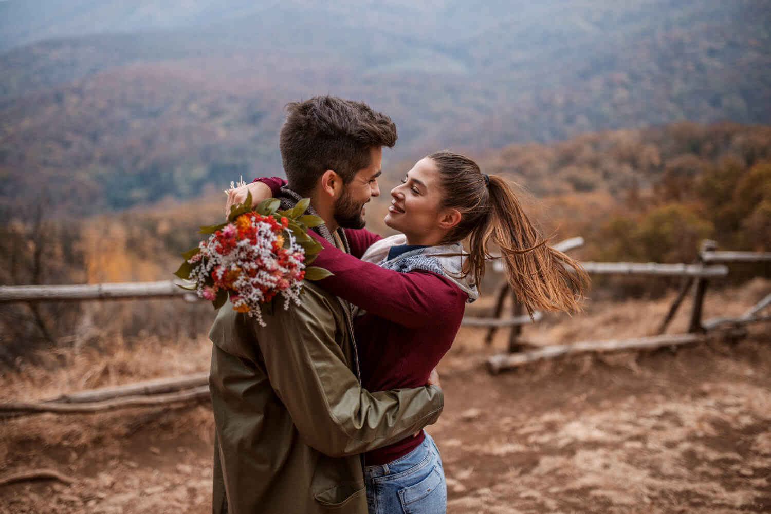 a couple with a flower bouquet is outside in nature hugging each other romantically