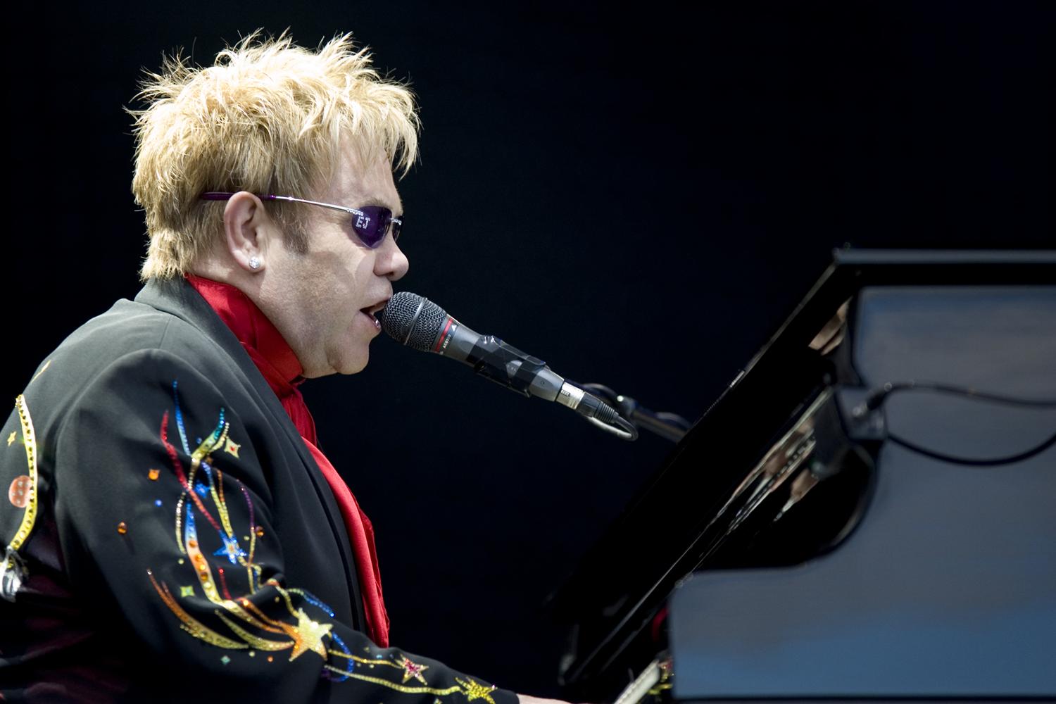 sir elton john sitting on a piano performing a song