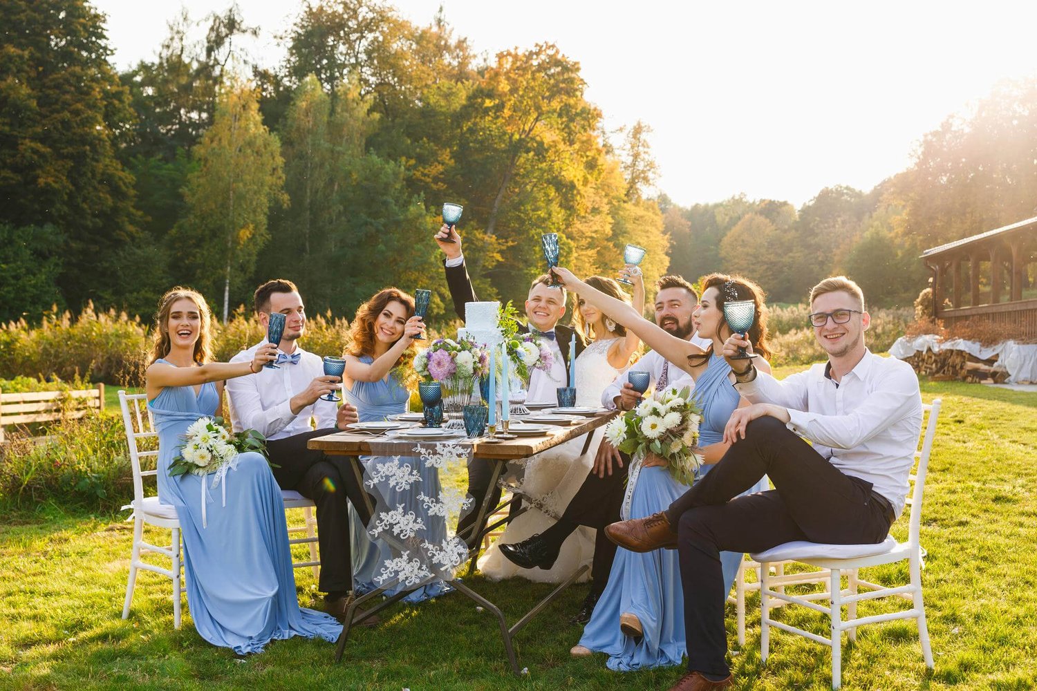 bride, groom, and wedding guests sit together outside on a table and celebrate