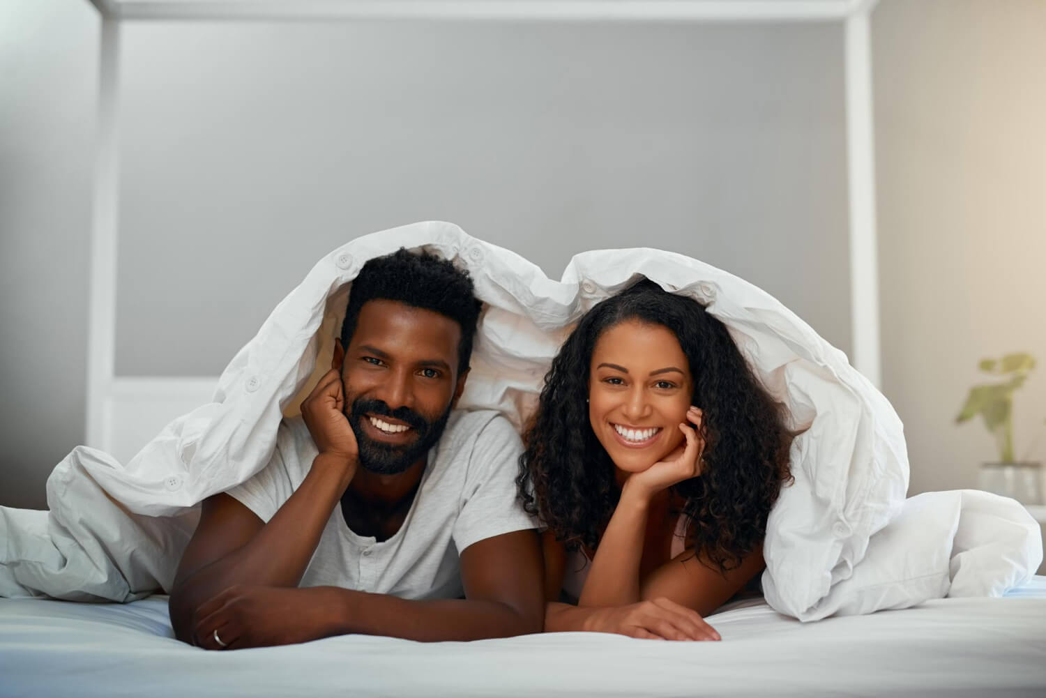 a man and a woman together in a bed under a blanket smiling into the camera