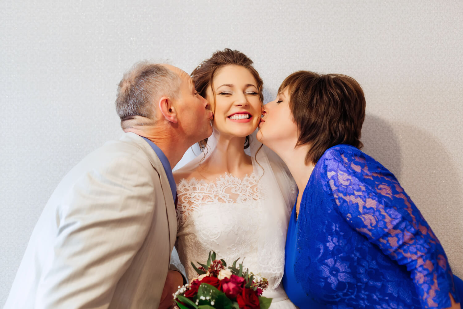 the two parents kissing the bride on her cheeks