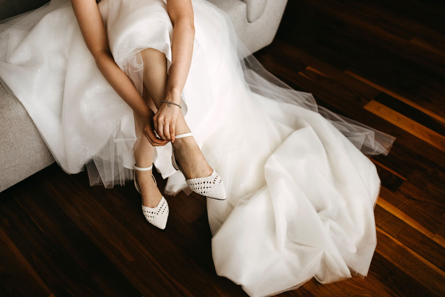 a bride is sitting down wearing a white wedding dress and putting on a shoe