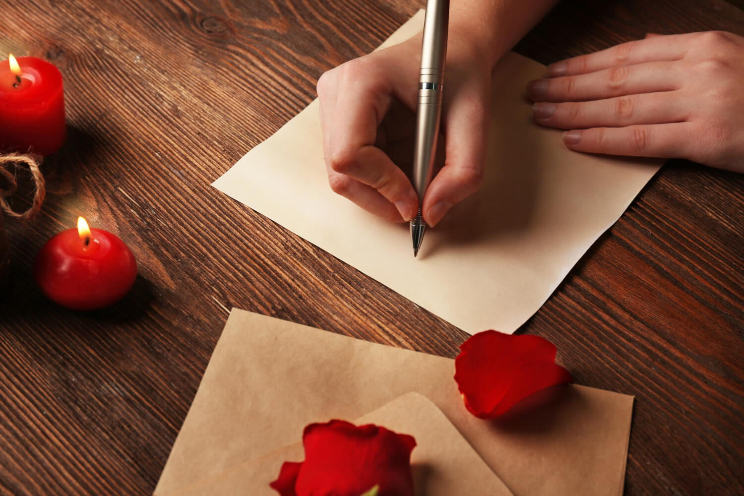 woman writing on a piece of paper next to two red candles and two red rose petals