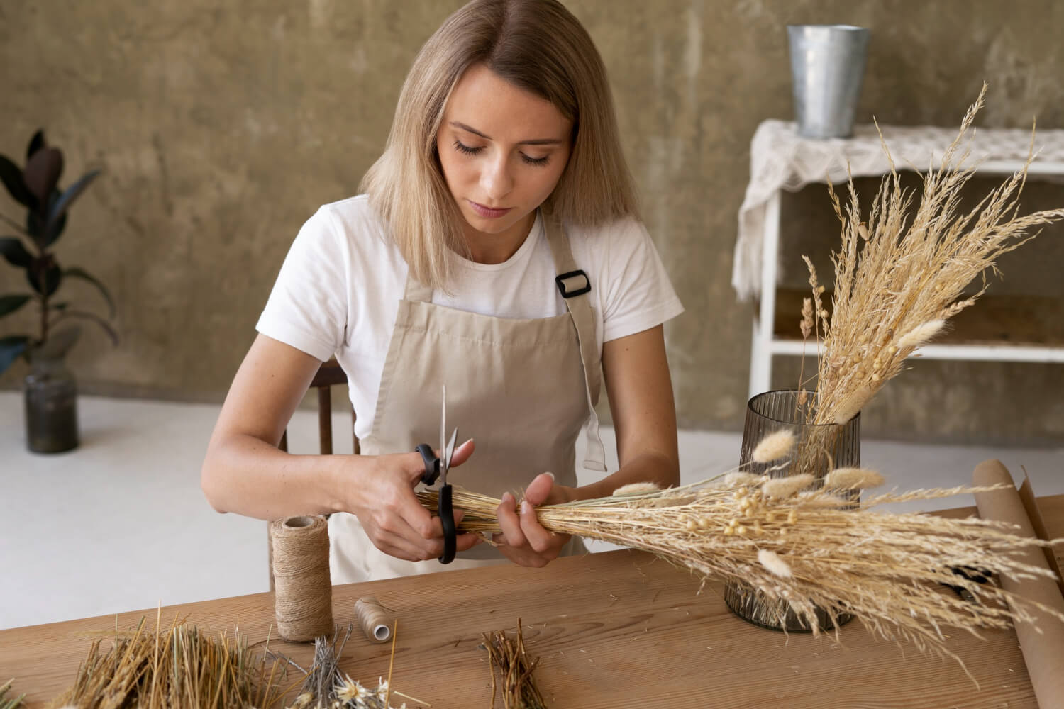 a woman is sitting on a table and is using scissors to cut dried flowers