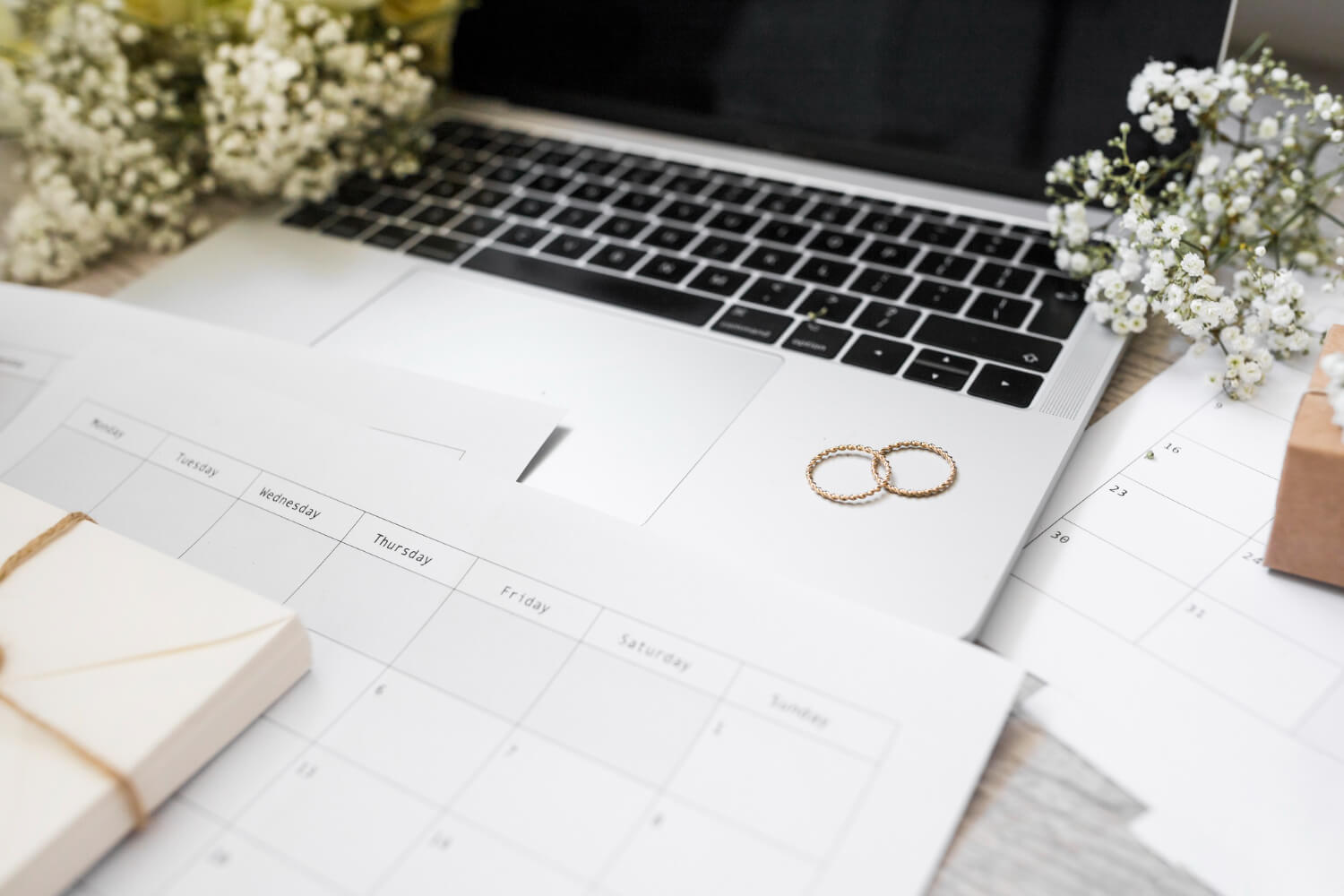 a desk with laptop, two wedding rings, calendar, and a gift