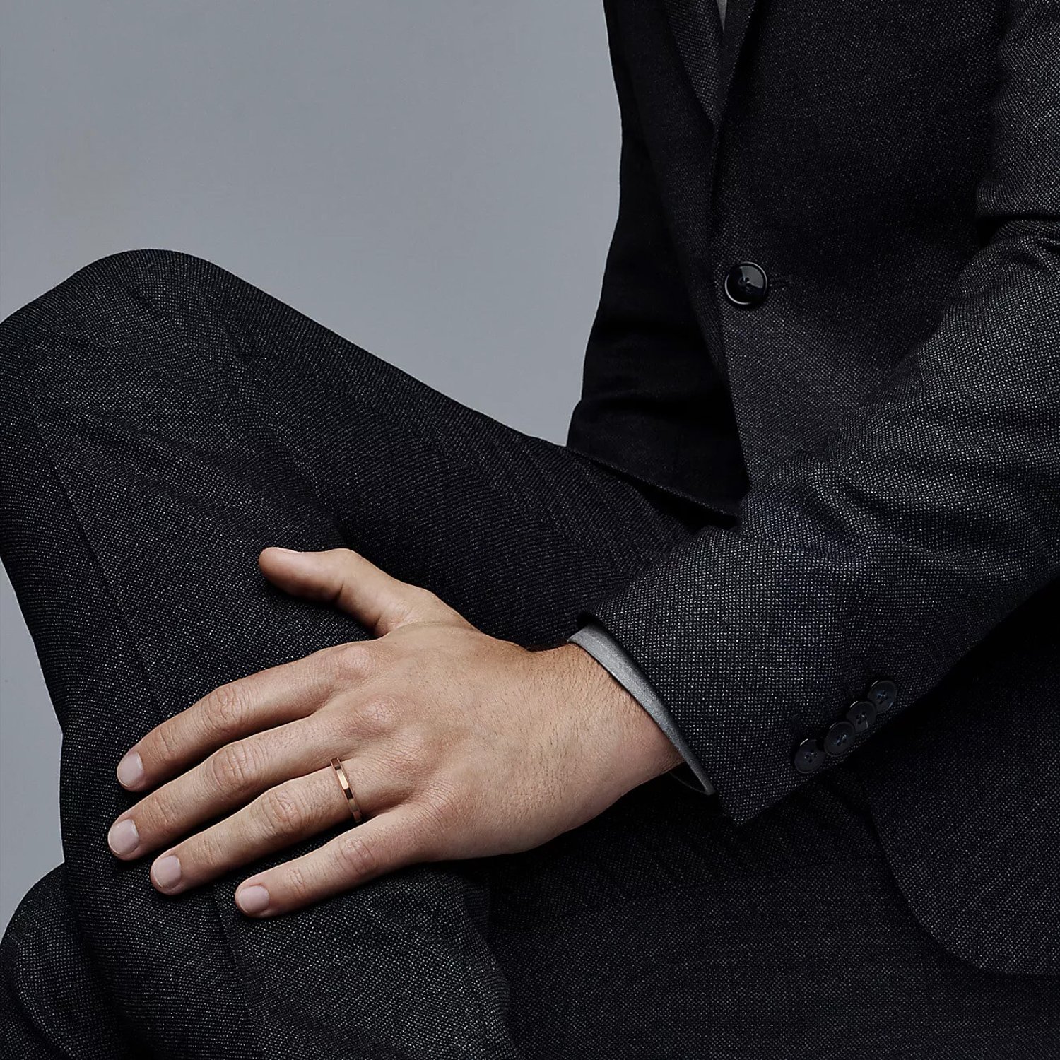 a man with a dark suit is wearing a rose gold ring on his left hand