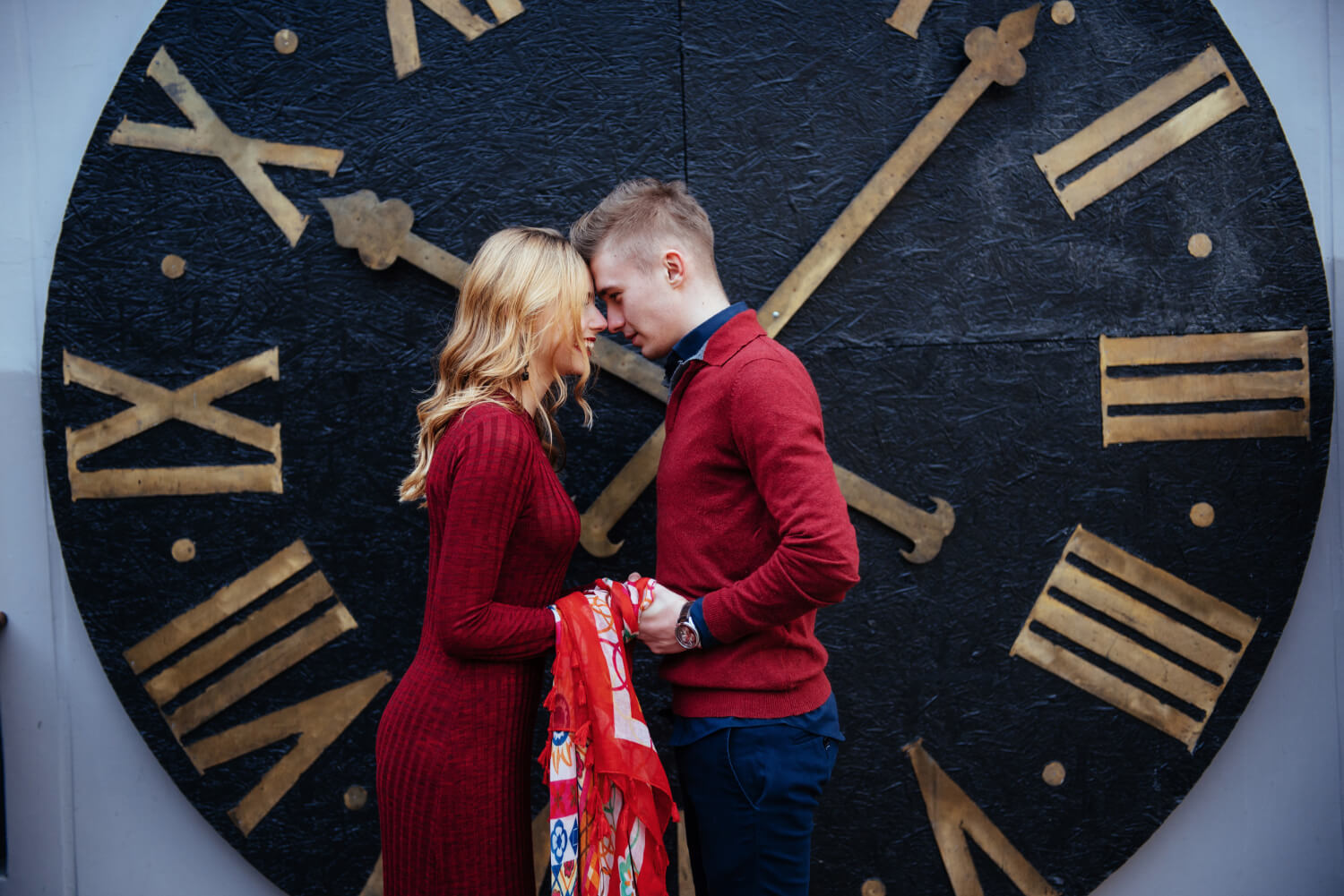 a young couple standing close together in front of a large clock