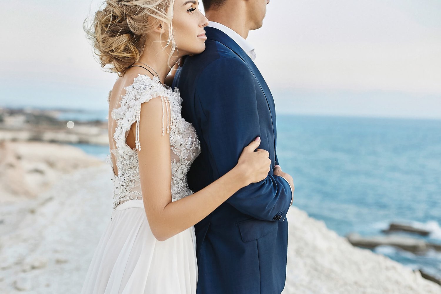 romantic wedding couple standing on the beach looking at the sea