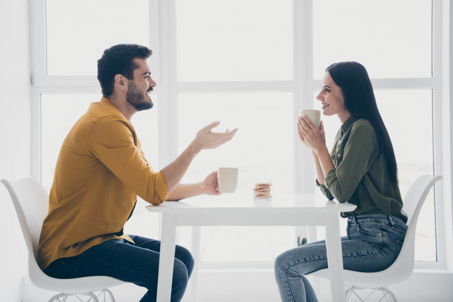 a man and a woman sitting on a table, drinking coffee, and talking