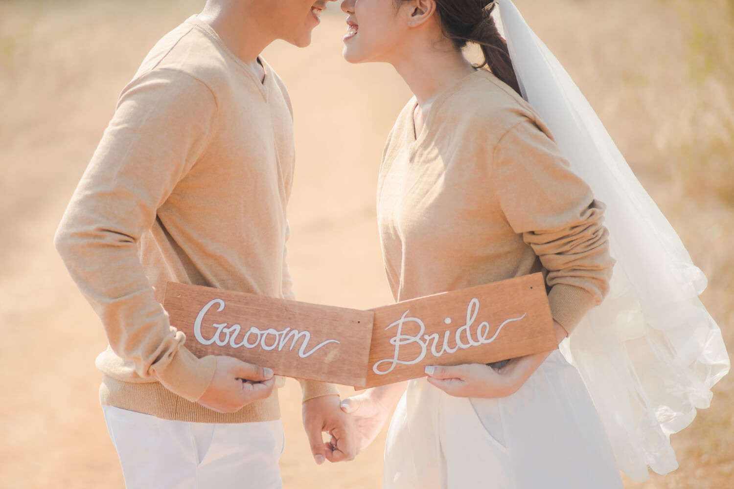 A couple tries to kiss while holding wooden signs that say groom and bride.