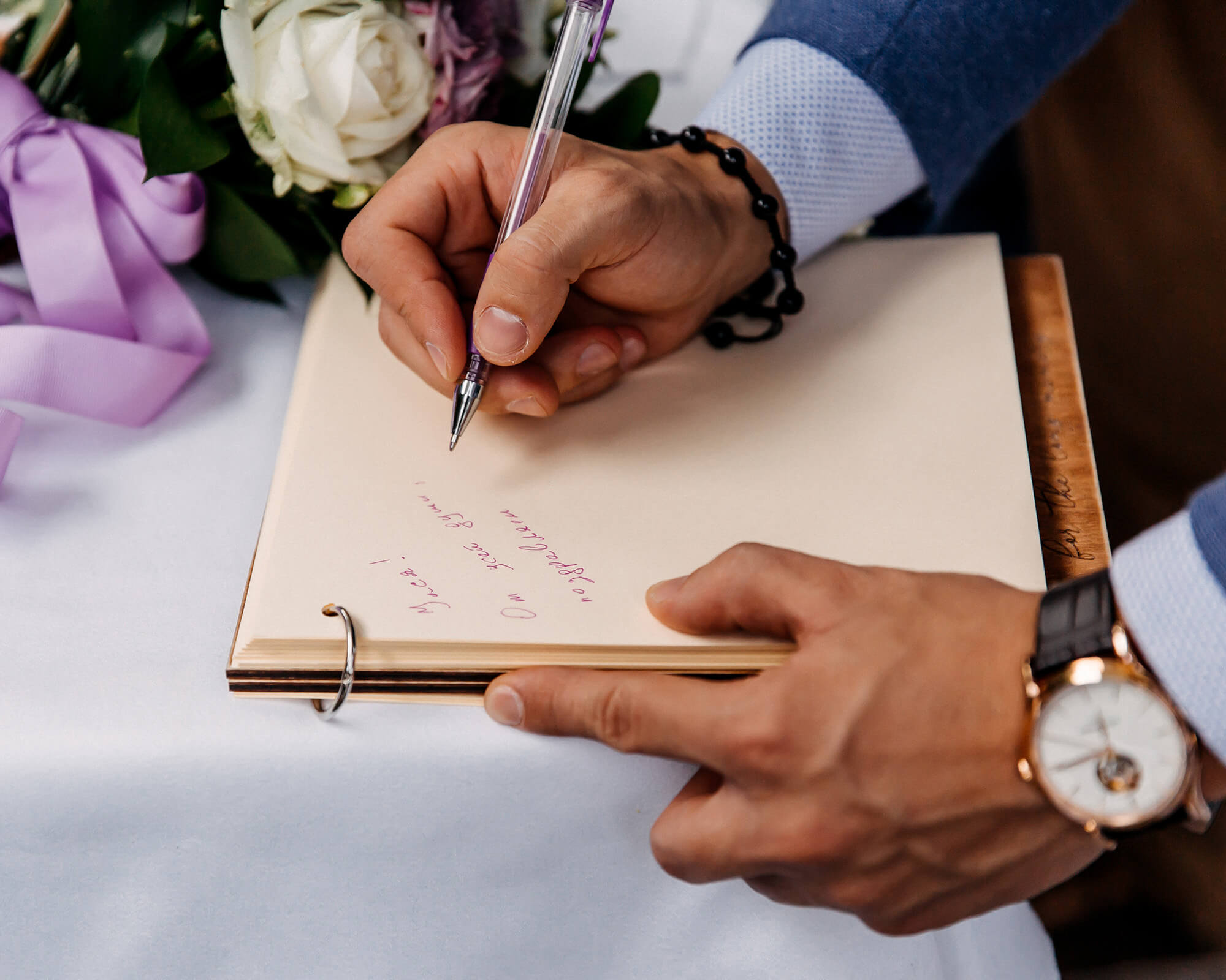 closeup of a man writing down a message in a wedding guest book