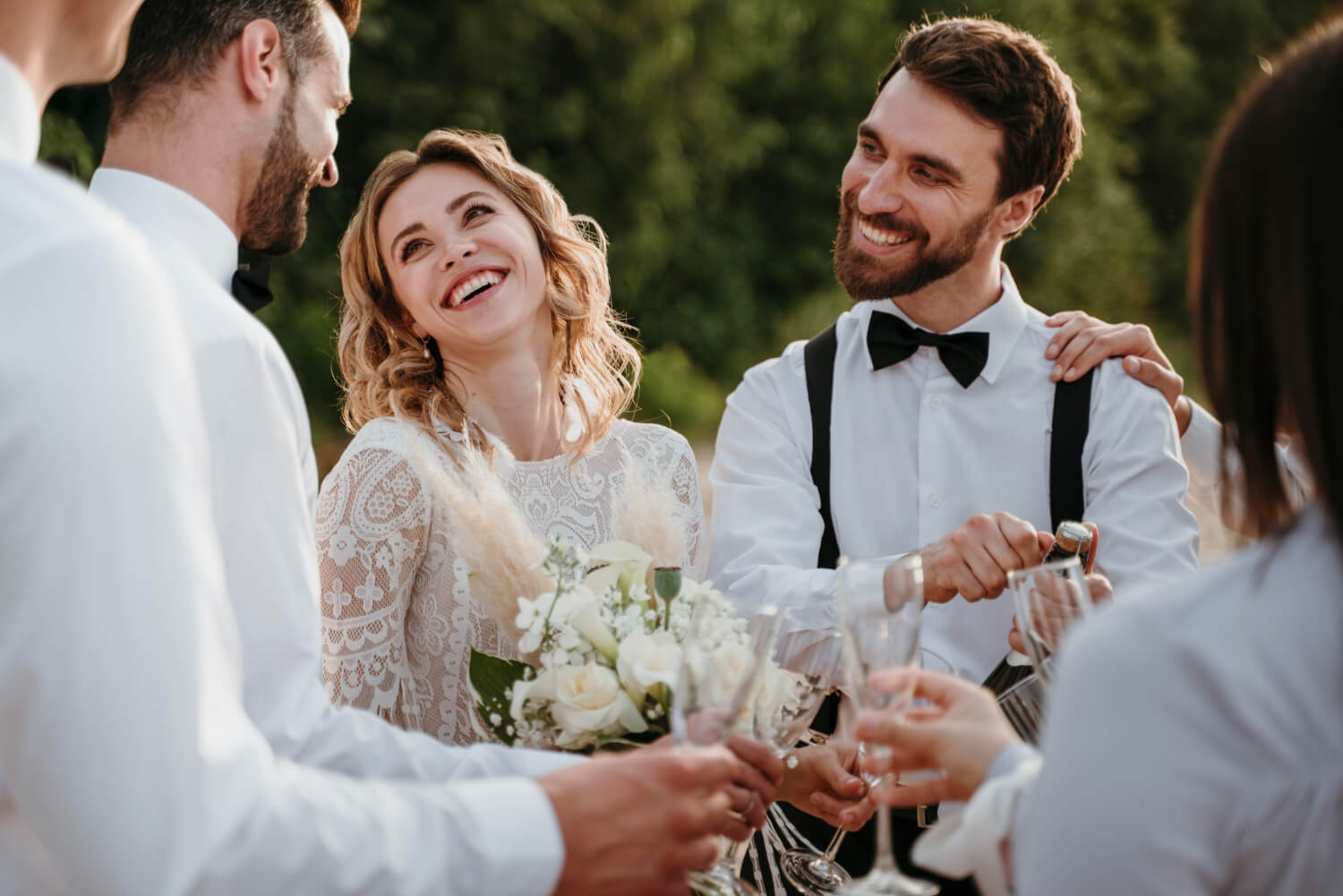 the bride and groom standing together with wedding guests laughing and drinking champagne