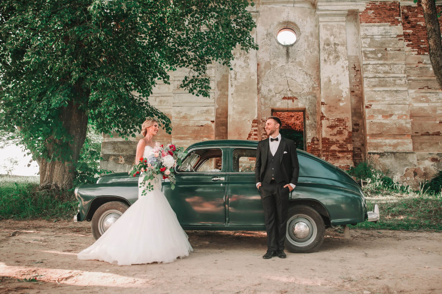 bride and groom next to an oldtimer car in front of an old building