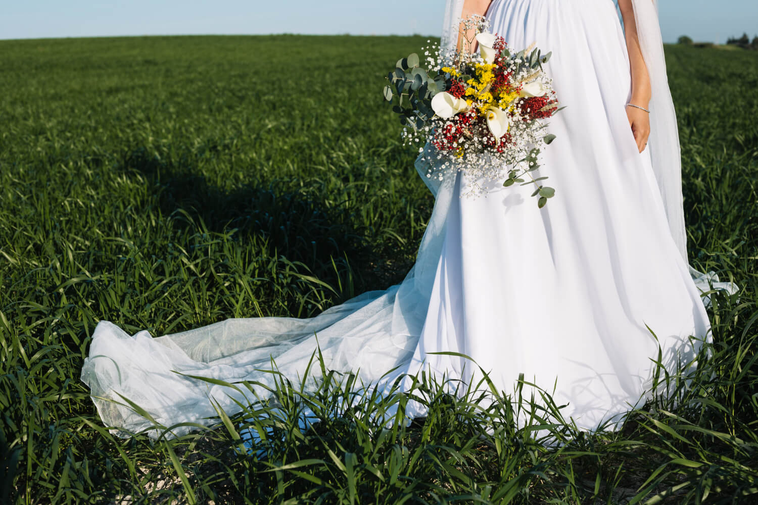 a bride holds a bouquet of wildflowers and stands on a large meadow